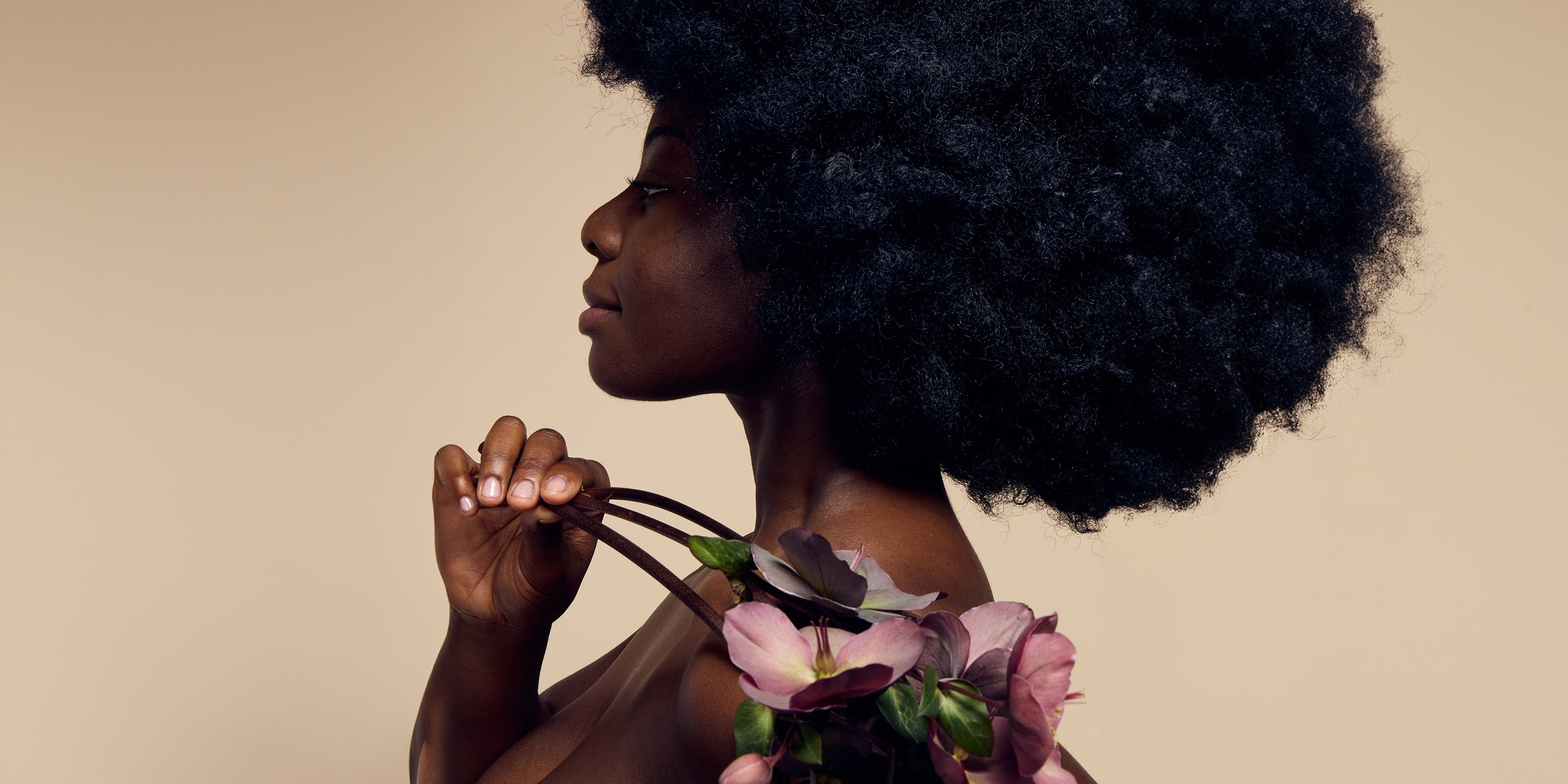 A model with black skin showcasing their glowing, radiant complexion achieved with James Read's Self Glow tanning products while holding a flower, emphasising the natural beauty of the results.